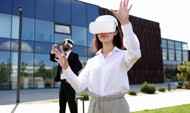 High quality photo of man and woman in business style and VR headset standing at modern glass building of office center. Virtual reality experience. Business people in technology. Work in metaverse.