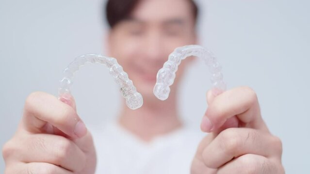 Young smiling man holding invisalign braces over white background studio, dental healthcare and Orthodontic concept