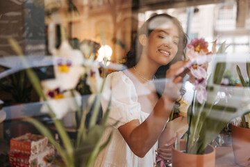 Beautiful young caucasian woman examines orchids in pots walking through store. Brunette loves to buy houseplants. Lifestyle concept