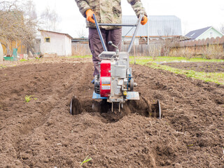 A man works the land in the garden with a cultivator, prepares the soil for sowing. farming concept