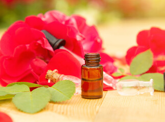 pink rose flower and glass of bottled essential oil or rose water with rose petals on wooden table, aromatherapy concept