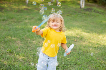 happy blond boy with long hair in a yellow T-shirt playing with soap bubbles