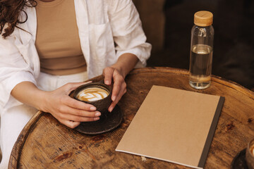 Image of caucasian girl wear white summer suit peeling off in street cafe. On table is cup of coffee, bottle of water and notebook. Modern lifestyle, people and youth concept