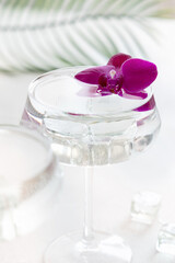 Transparent cocktail in a glass decorated with purple orchid flowers close up