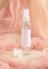 Fototapeta na wymiar One pump dispenser bottle near white orchid flowers againts light pink tulle. Mockup