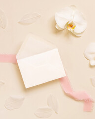 Obraz na płótnie Canvas Wedding envelope near white orchid flower and silk ribbons on yellow, mockup