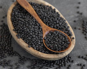 Bowl of dry black lentils beans with a spoon on grey table, protein source for vegetarian diet