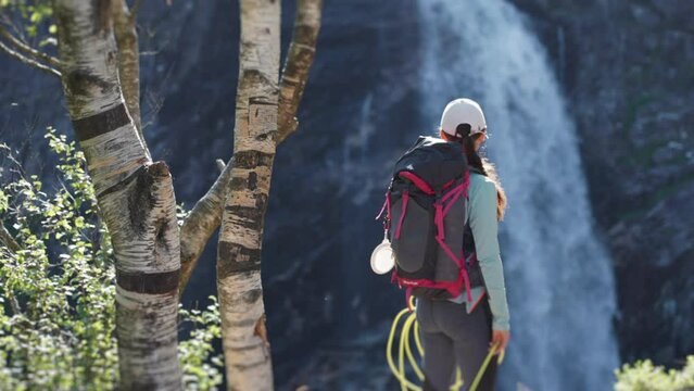 A female hiker standing at the end of the rocky trail. A waterfall falling into the deep gorge is before her.