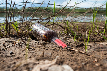Abandoned garbage in nature. Environmental damage caused by garbage pollution. Left glass bottle among the grass against the background of the river