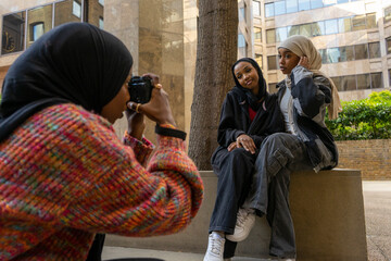 Young woman photographing friends wearing hijabs in city - obrazy, fototapety, plakaty