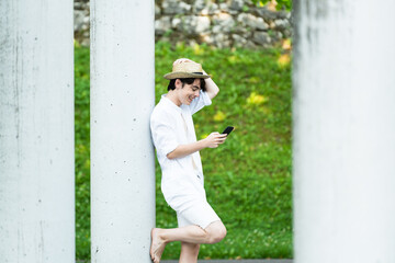 Cute teenager standing and using phone against column. Positive boy using social media