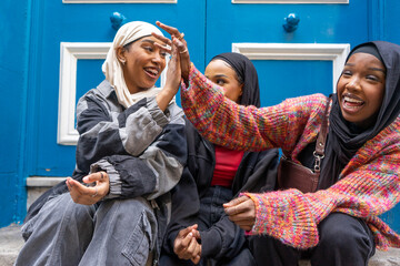 Three smiling women wearing hijabs sitting in front of blue door