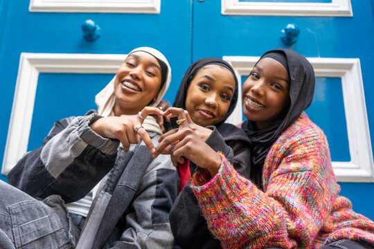 Portrait of three smiling women wearing hijabs showing heart gesture