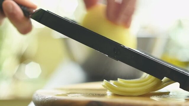 Potatoes being thinly sliced, slow motion.

