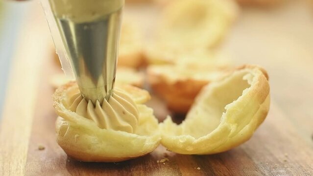 Confectioner filling the profiteroles with caramel cream.
