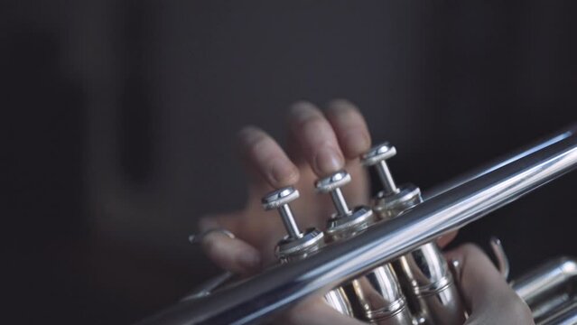 Fingers of a trumpet player playing a silver plated trumpet on the valves in slow motion