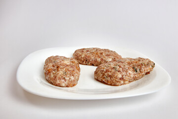 Raw cutlets from minced meat on a white plate.