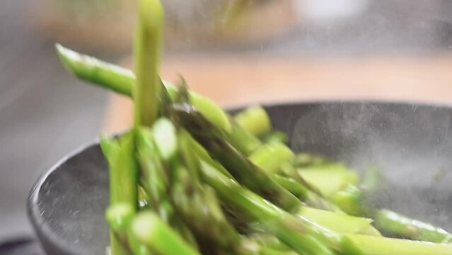 Cooking and stirring green asparagus in a frying pan.
