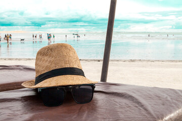Hat and sunglasses on a beach chair with the sea in the background and blue sky. Brazilian beach....