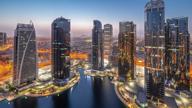 Tall residential buildings at JLT district aerial night to day transition panoramic timelapse, part of the Dubai multi commodities centre mixed-use district. Skyscrapers before sunrise