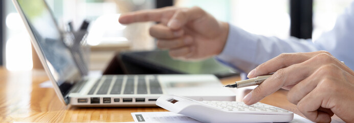 Financial or accounting professionals use a laptop to analyze the company's revenue-expenses graph to prepare for presentation to the chief executive and partner, Calculate data with a calculator.