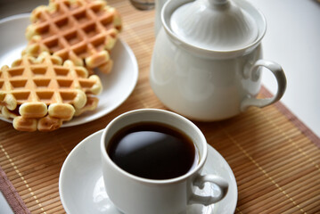 Obraz na płótnie Canvas Tea couple with Viennese waffles on a mat. Tea party with waffles. A porcelain cup and saucer on a mat.