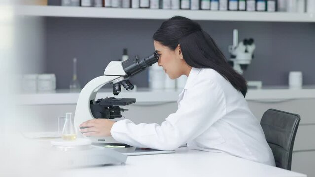Female pathologist analyzing medical samples while doing experiments to develop a cure. Microbiologist conducting forensic research. Young scientist using a digital tablet and microscope in a lab.