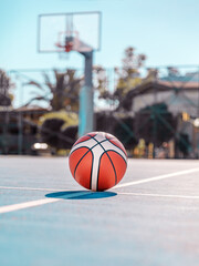 Orange basketball on the markup blue court against the backdrop of a basketball hoop outside. Team...