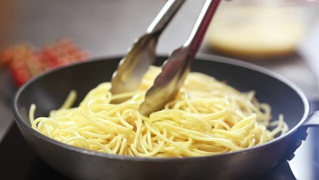 Cooking and stirring spaghetti in a frying pan.
