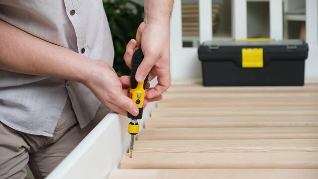 The furniture assembler assembles the bed, twists the screws on the wooden slats.