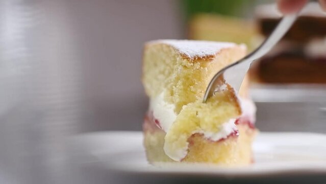 Fork breaks off a piece of classic Victoria Sponge cake.
