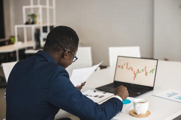 African American men in a business suit are working on a laptop studying stock market charts and technical analysis.