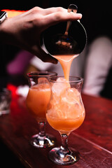 Close-up of a bartender's hand. Pouring an orange alcoholic cocktail into a glass with a long stem. Rest in a nightclub, bar, restaurant