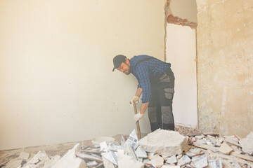 A man in a work suit with a baseball cap cleans up in an apartment under renovation, picks up...
