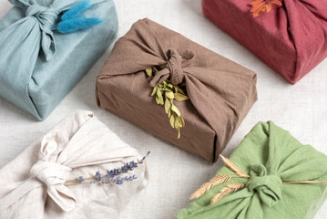 Gifts wrapped in linen fabric with dried flowers. Furoshiki colored gifts. Zero waste concept. Reusable eco-friendly packaging. Selective focus.