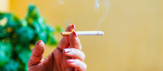 Middle age woman smoking cigarette.Close up of a female hand holding cigarette.copy space.Blurred image.Side view.Banner,advertisement.