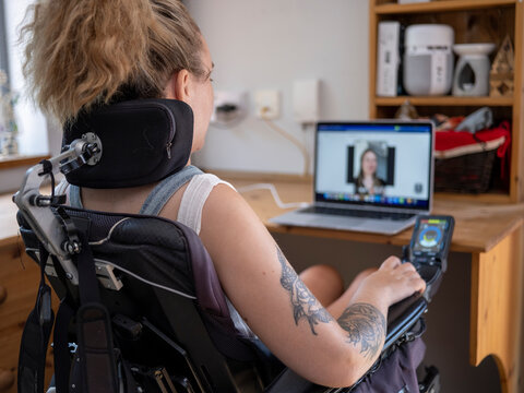 Woman in electric wheelchair having video call on laptop