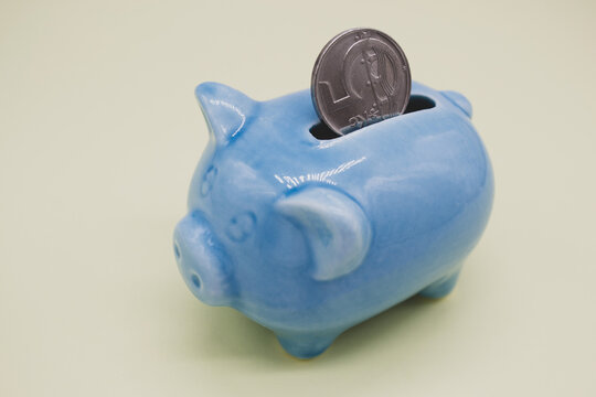 Blue ceramic piggy bank with a suspicious look and a coin of 5 CZK in the hole on a yellow background. Copy space