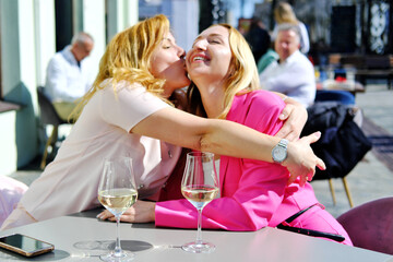 Two beautiful adult blonde women met at a table in a cafe and hug when they meet
