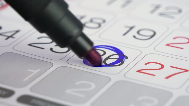 Calendar date. Noting the day on a paper calendar planner with a blue marker