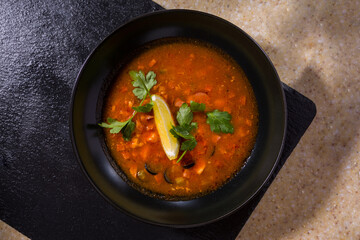 A plate of red soup with lemon, parsley, olives