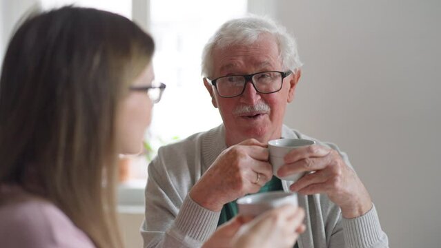 Adult daughter visiting her senior father at home and having coffee together, talking.