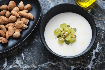 Ajoblanco or spanish white gazpacho served with grapes in a black bowl, elevated view on a black marble background, horizontal shot