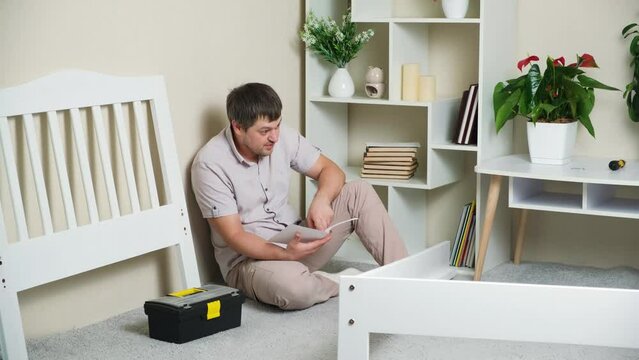 A puzzled father studies a complex instruction for assembling a children's bed.