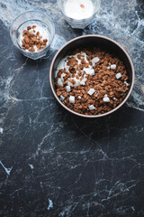 Bowl of chocolate granola served with addition of yogurt, high angle view on a black marble background, vertical shot with copyspace