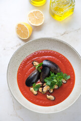 Plate of tomato cream-soup with mussels on a beige marble background, vertical shot, high angle view