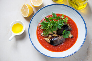 Tomato cream-soup with mussels and parsley served in a white plate, horizontal shot on a beige stone background, elevated view
