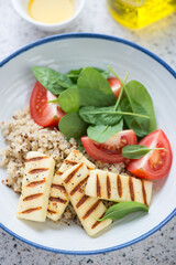 Fototapeta na wymiar Quinoa with grilled halloumi, fresh spinach and red tomatoes, vertical shot, closeup, selective focus