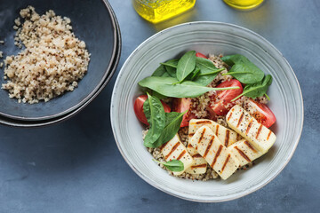 Plate with grilled haloumi cheese, fresh spinach, quinoa and tomatoes, elevated view on a grey concrete background, horizontal shot