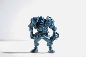 A figurine of an aggressive and vicious bald warrior in armor with a skull stands on a white background